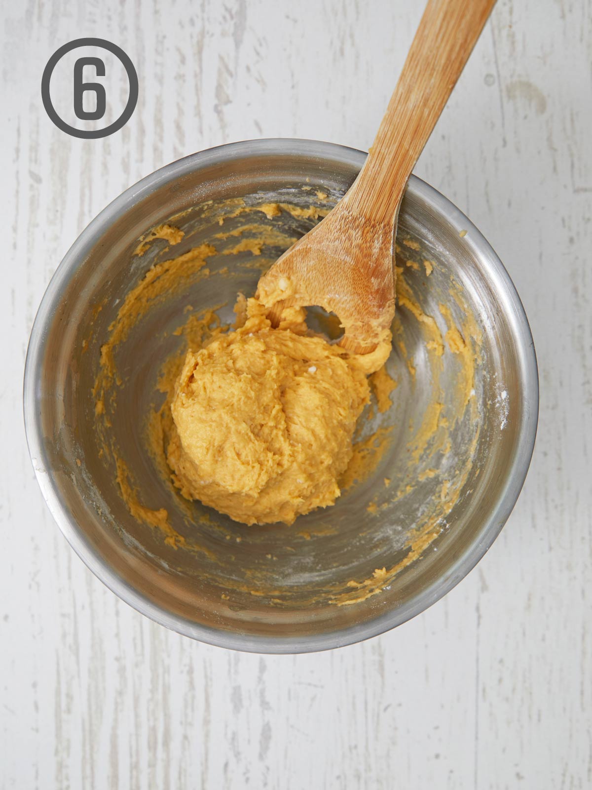 A wooden spoon is being used to mix the dough for pumpkin dinner rolls in a bowl.
