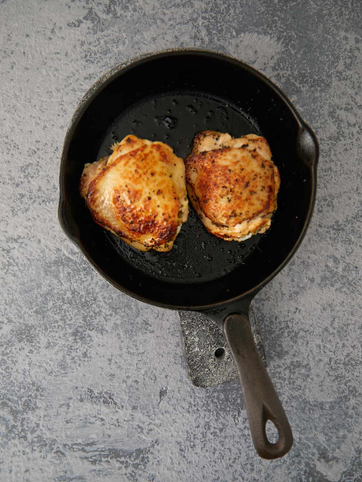 Golden brown skin on chicken in cast iron skillet.