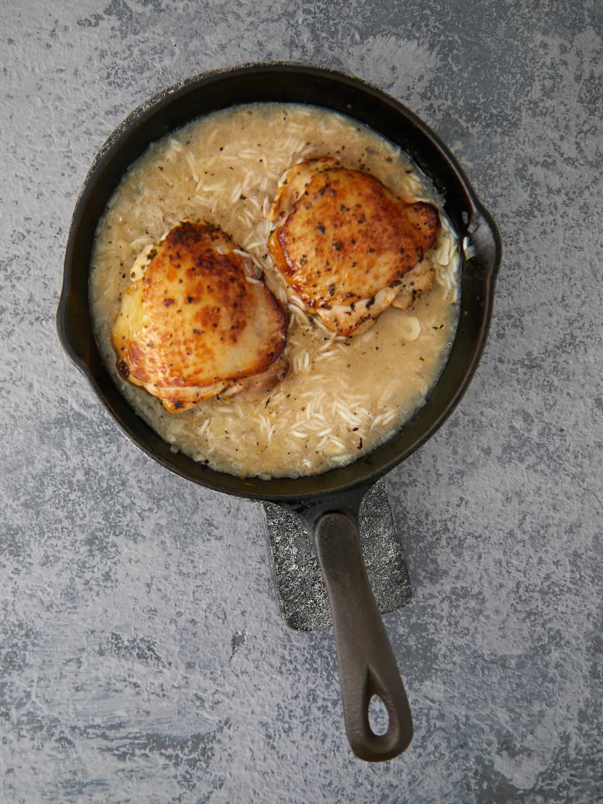 Skillet with chicken thighs nestled in with the rice.