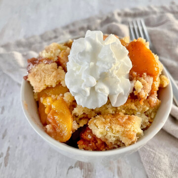 A bowl of peach cobbler with whipped cream.