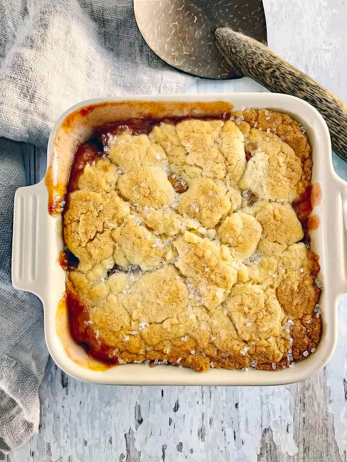 Baked cobbler with golden brown crust and bubbled up caramelized peach juice at edges.