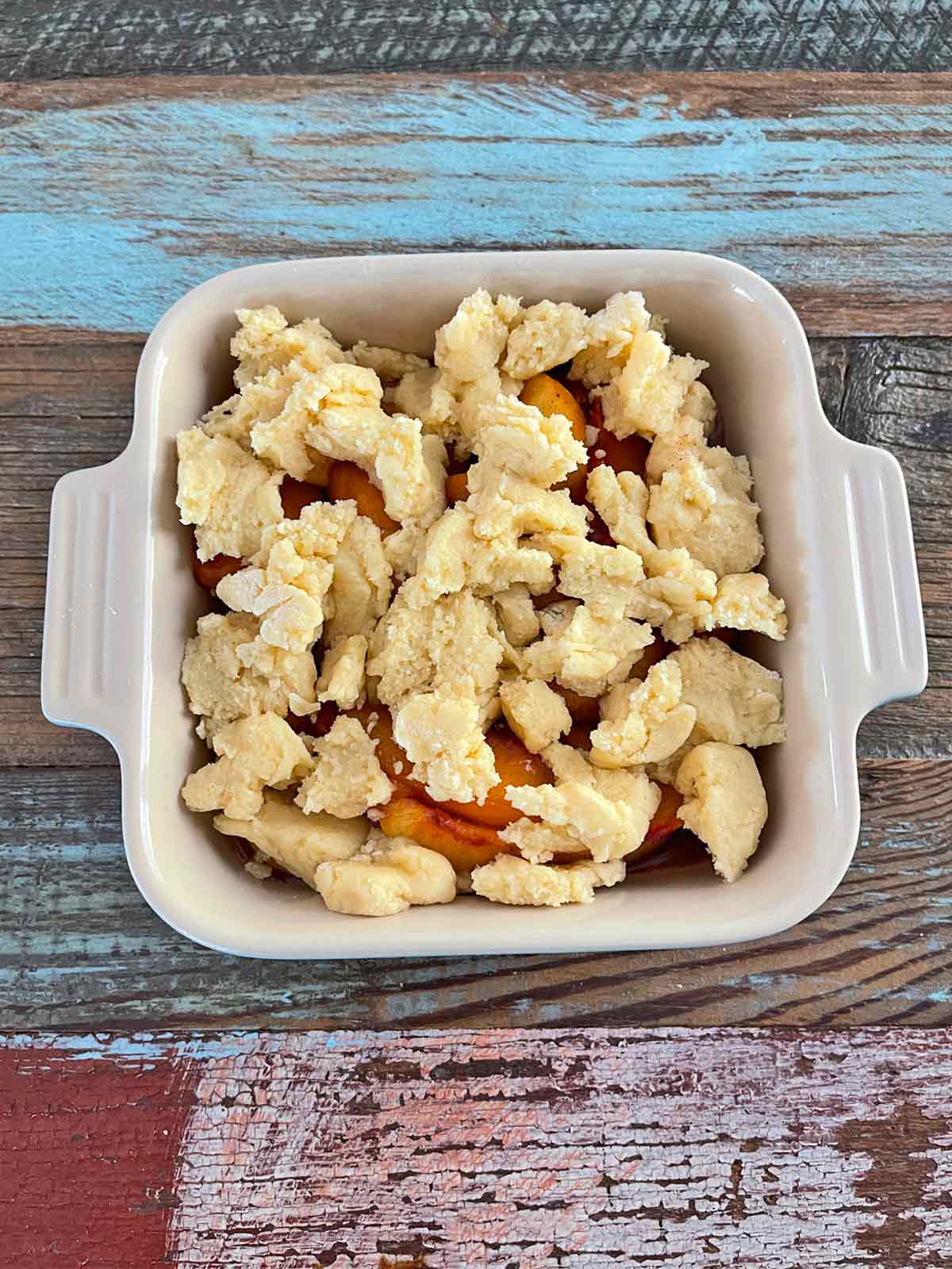 Baking dish with peaches and crumbled raw dough on top.