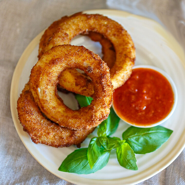 A plate of fried mozzarella onion rings with fresh basil and marinara sauce for dipping.