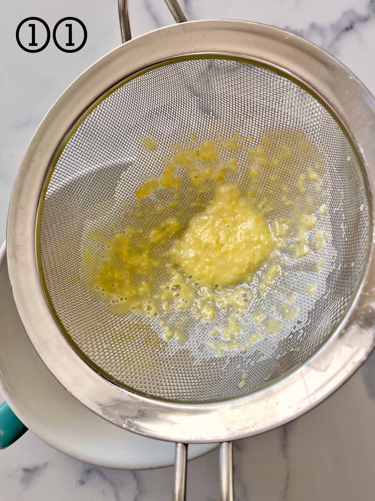 A strainer with a yellow liquid and mint chocolate chips mixed in it.