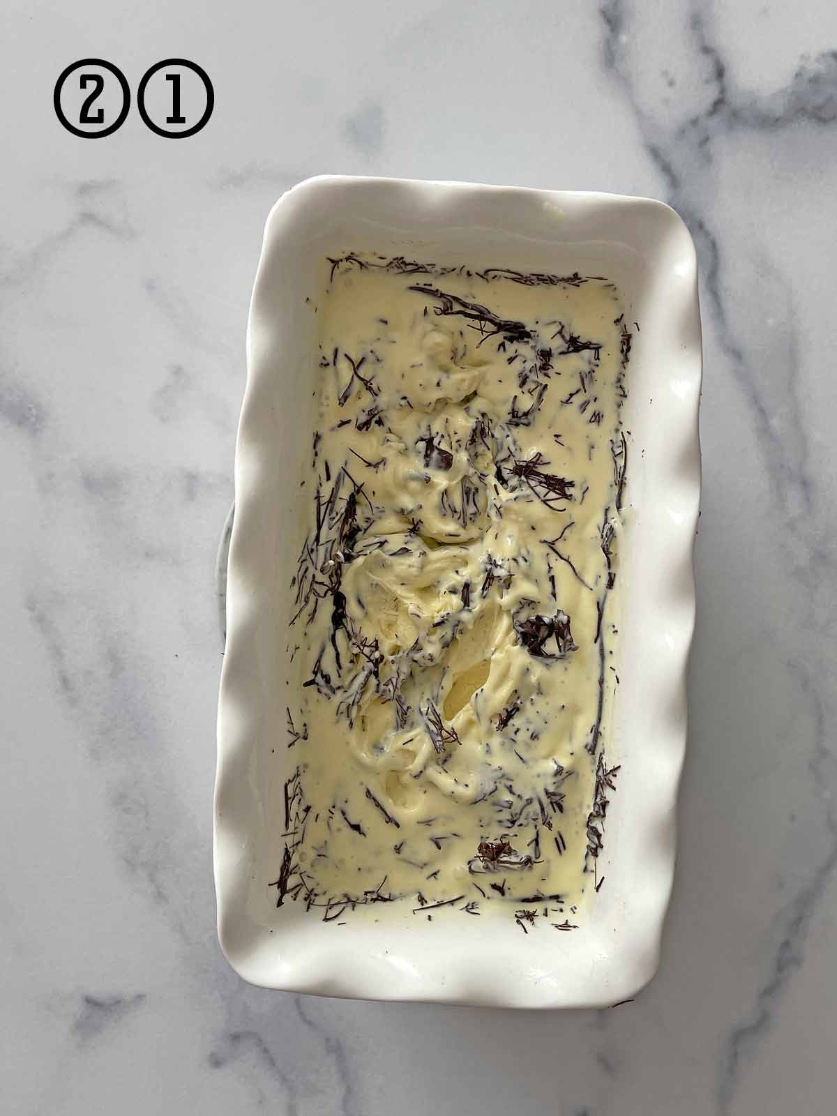 A bowl of mint chocolate chip ice cream on a marble table.