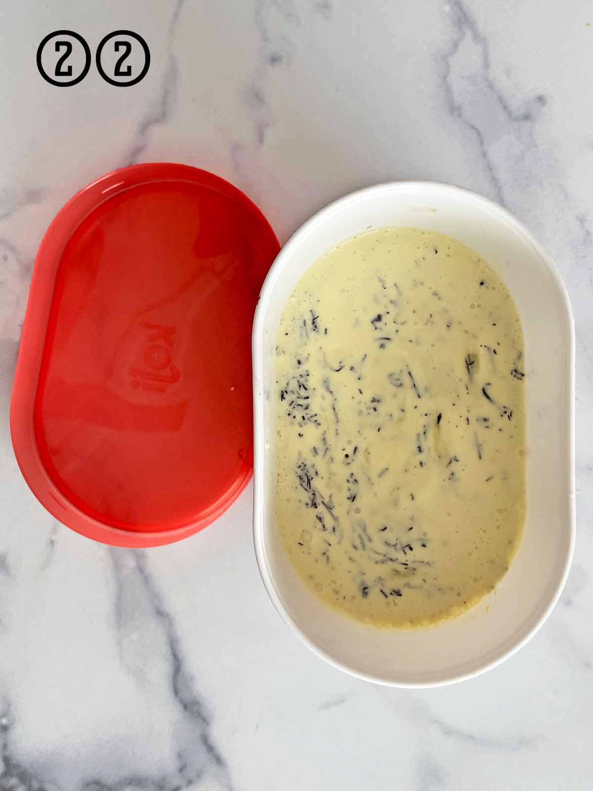 A bowl of ice cream with a red lid next to it, filled with mint chocolate chip ice cream.