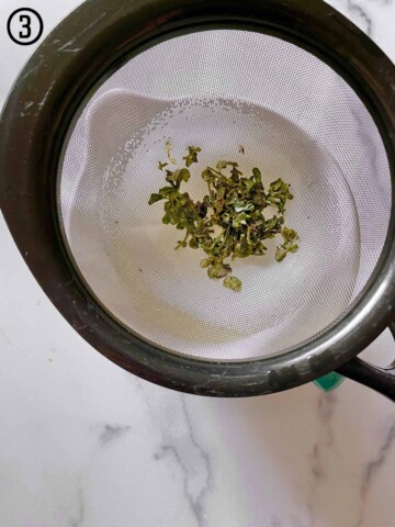 A strainer filled with green mint leaves.