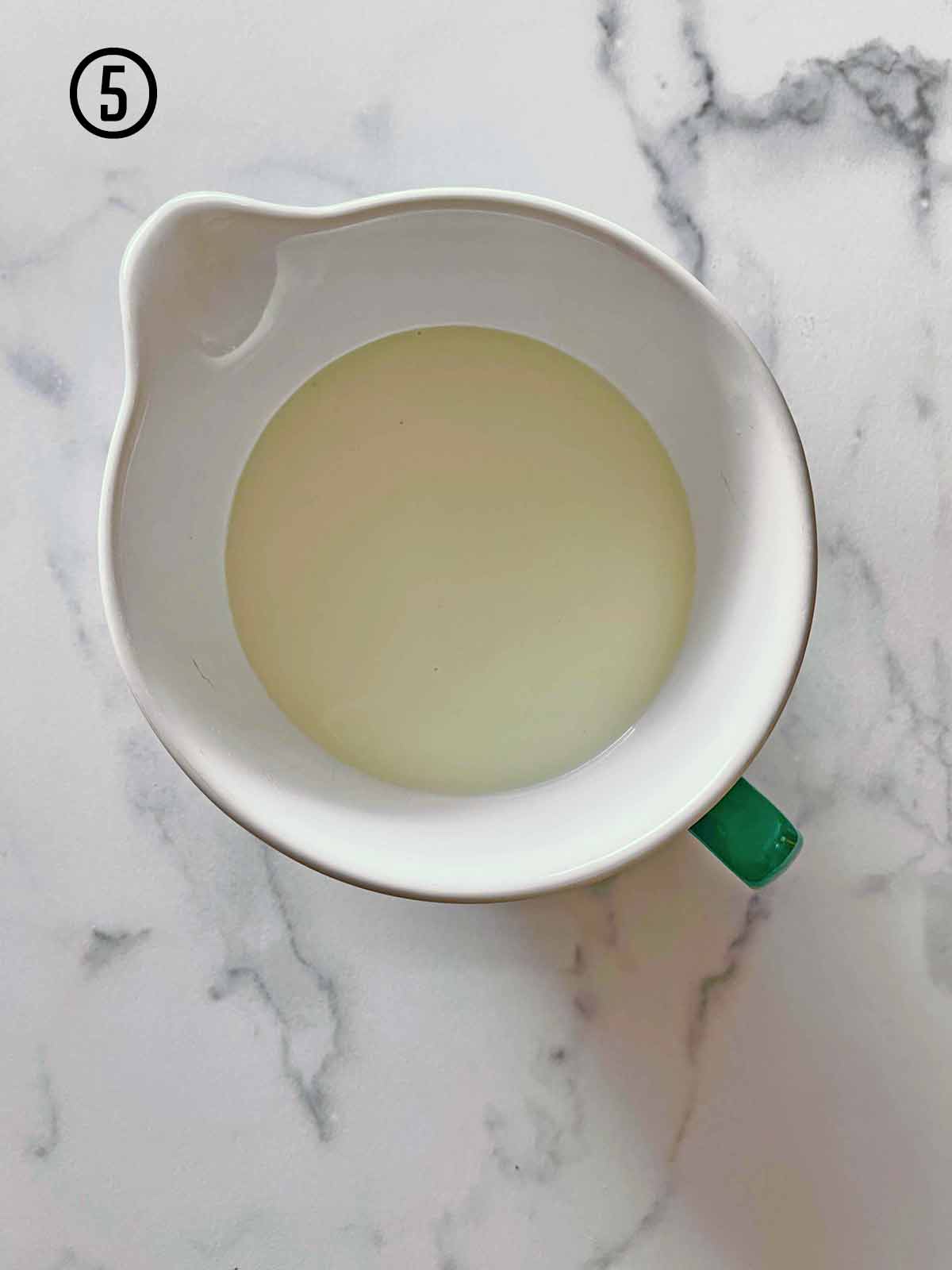 A white bowl filled with mint chocolate chip ice cream base on a marble counter.