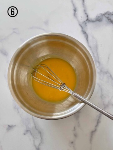 A whisk in a bowl of egg yolks.