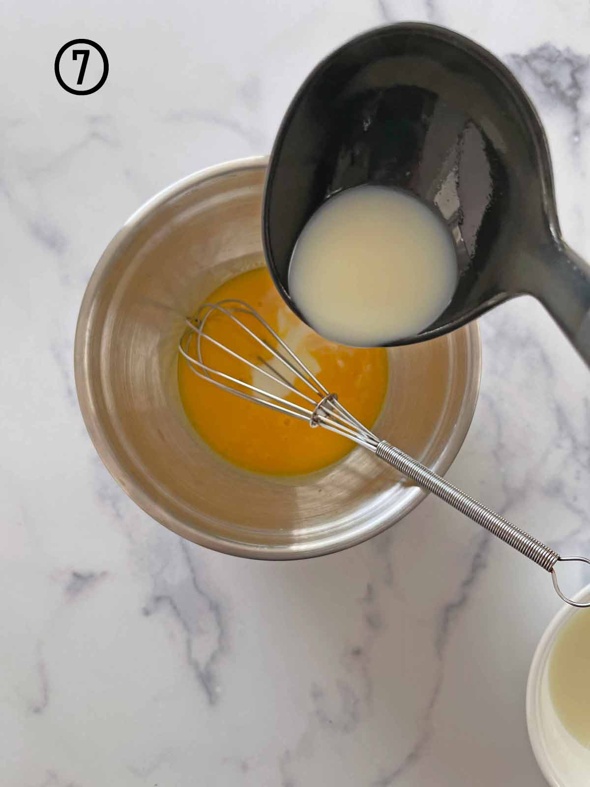 A bowl with a whisk and an egg in it, preparing mint chocolate chip ice cream.