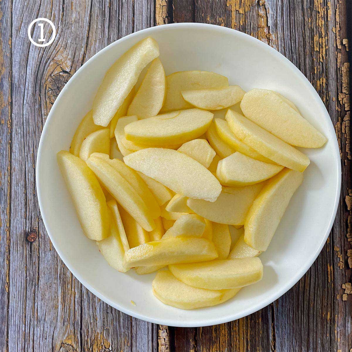 Easy Apple Pastry Recipe (Strudel): Sliced apples in a white bowl on a wooden table.