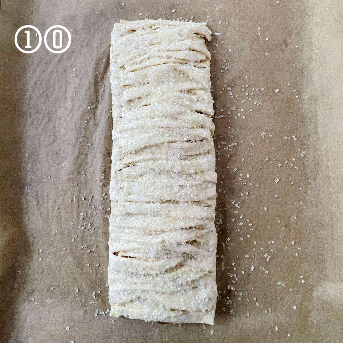 An apple strudel, made from a simple and easy puff pastry recipe, is resting on a baking sheet.