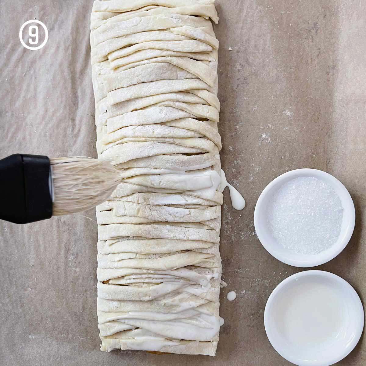 An easy apple strudel is being made using a brush to work with puff pastry dough.
