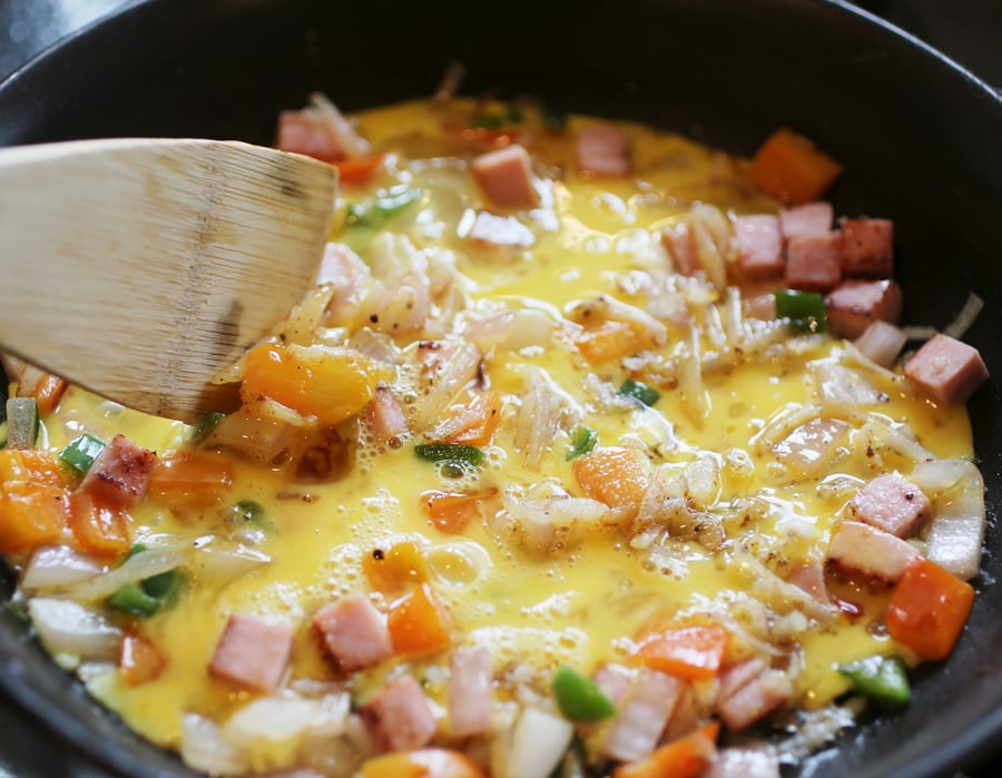 Adding eggs to skillet with ham and vegetables and scrambling