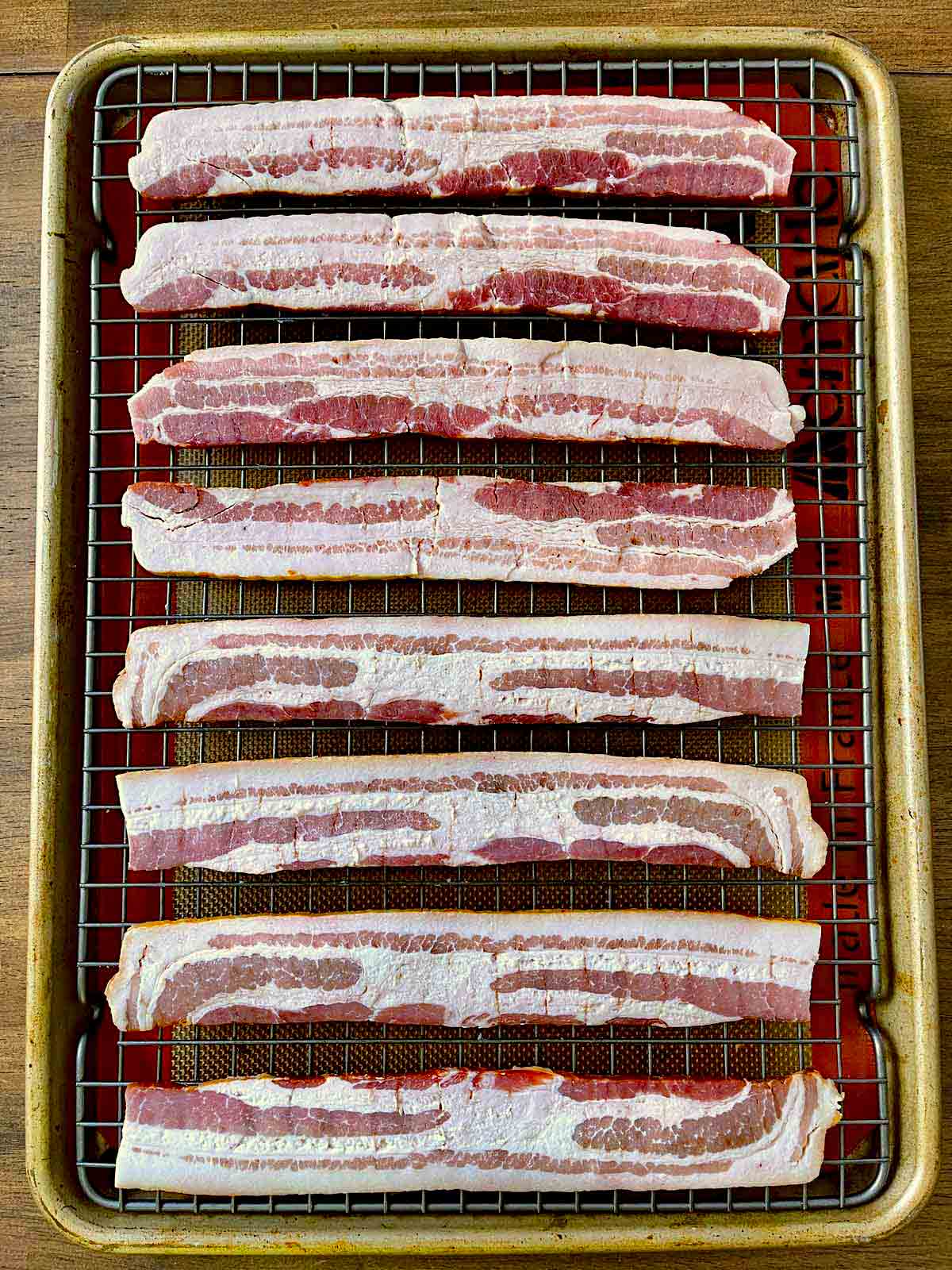 Baking sheet with bacon slices lying on wire rack.