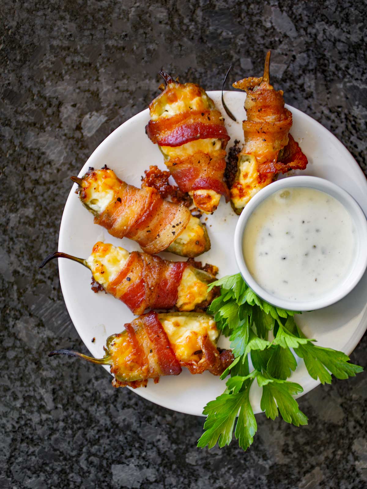 Plate of bacon wrapped jalapeño poppers with ranch dressing on the side.