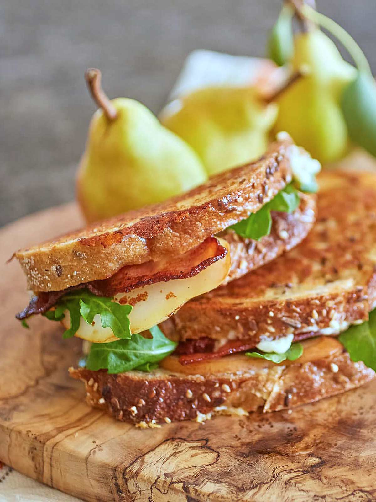 Serving board with a grilled cheese sandwich with bacon and fresh pear slices.