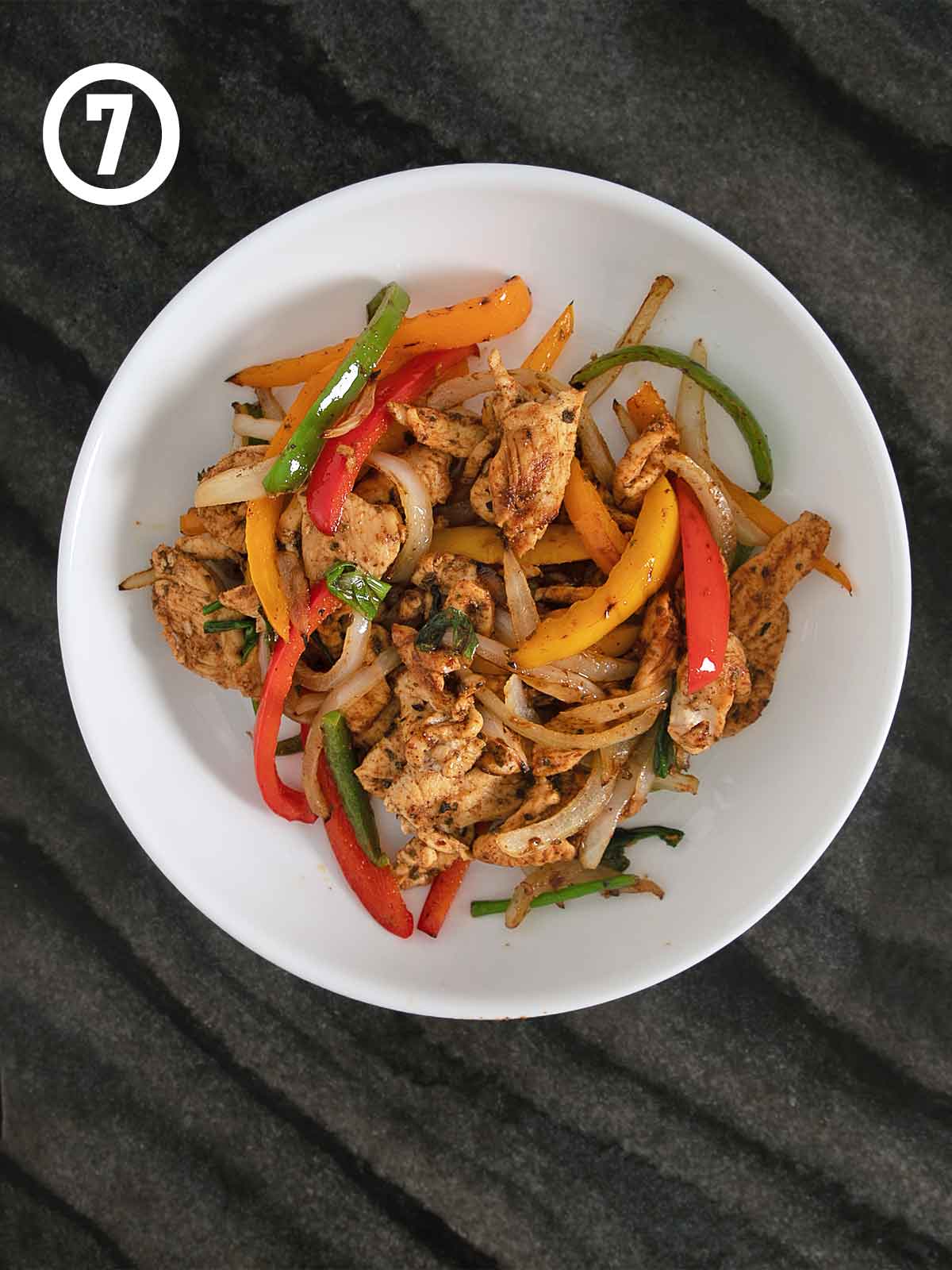 Grilled chicken fajitas with peppers and onions in a white bowl.