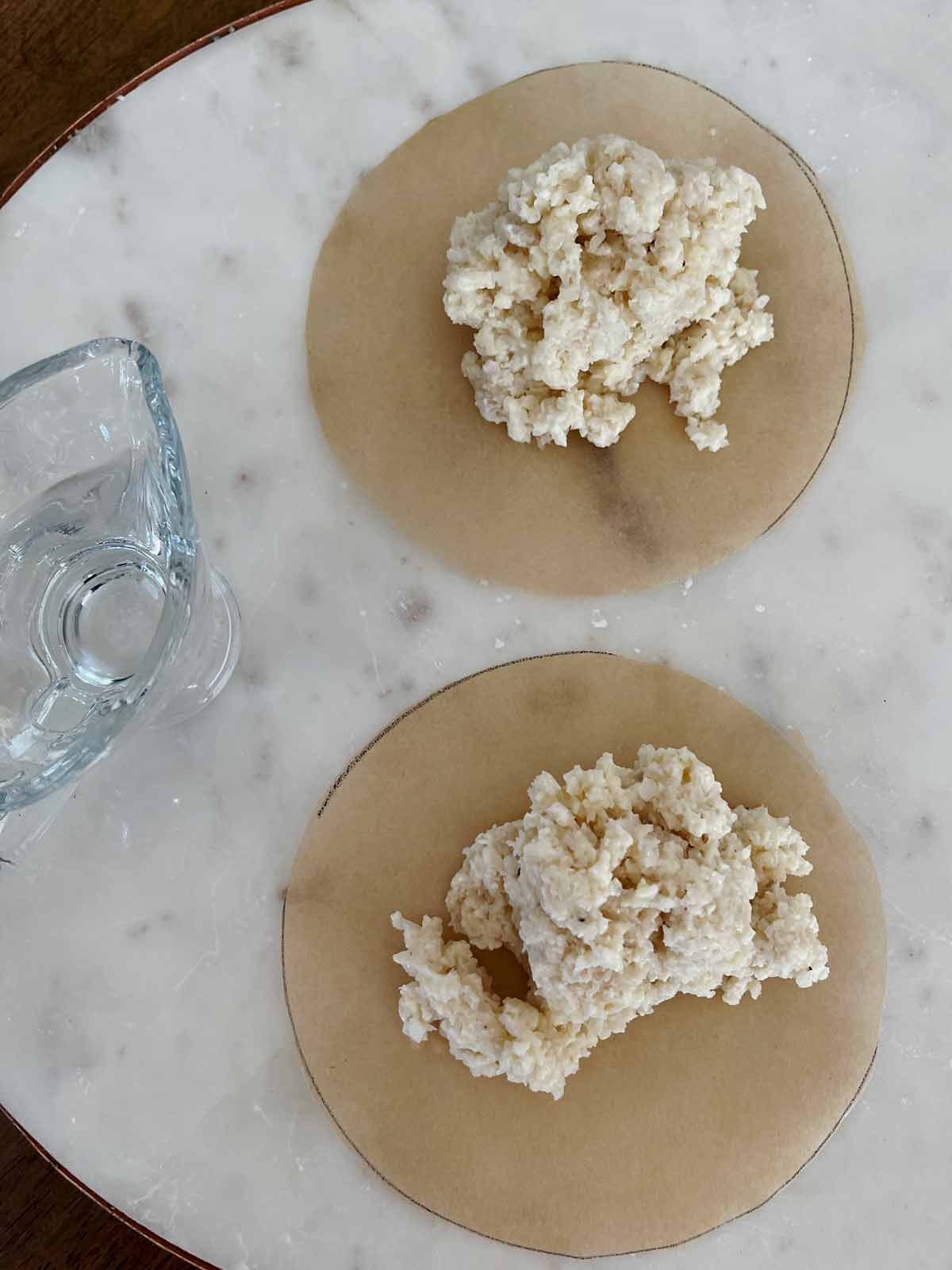 Cauliflower crust divided and placed on two rounds of parchment paper.