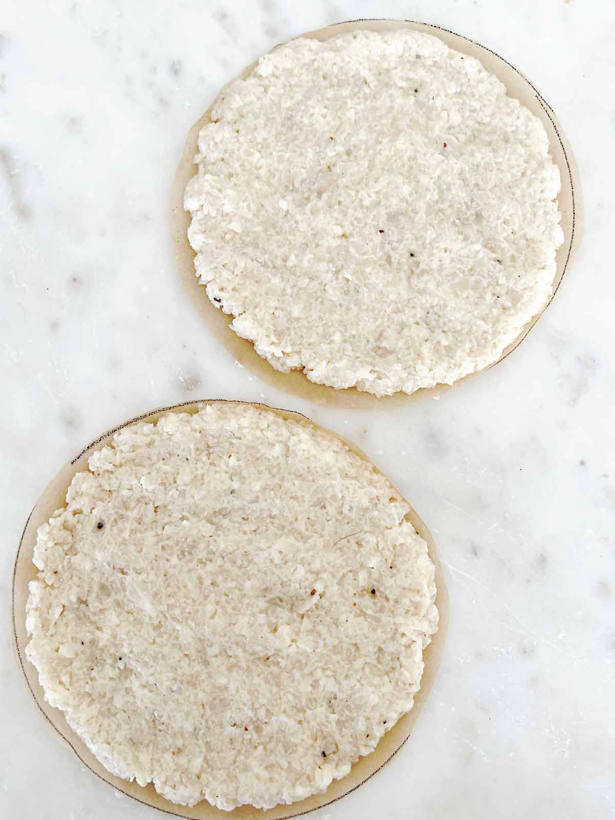 Balls of dough flattened out to cover the circle of parchment.