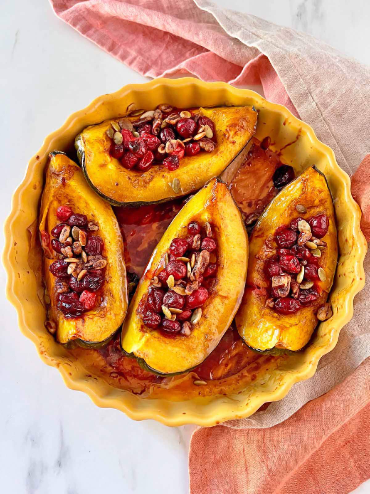 Baking dish with foru wedges of cooked acorn squash with cranberries.