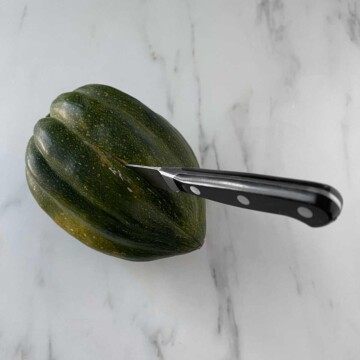 Acorn squash with knife sticking in side.