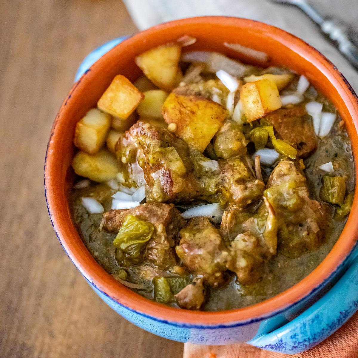 Blue soup bowl with hatch green chile Verde over roasted potatoes.
