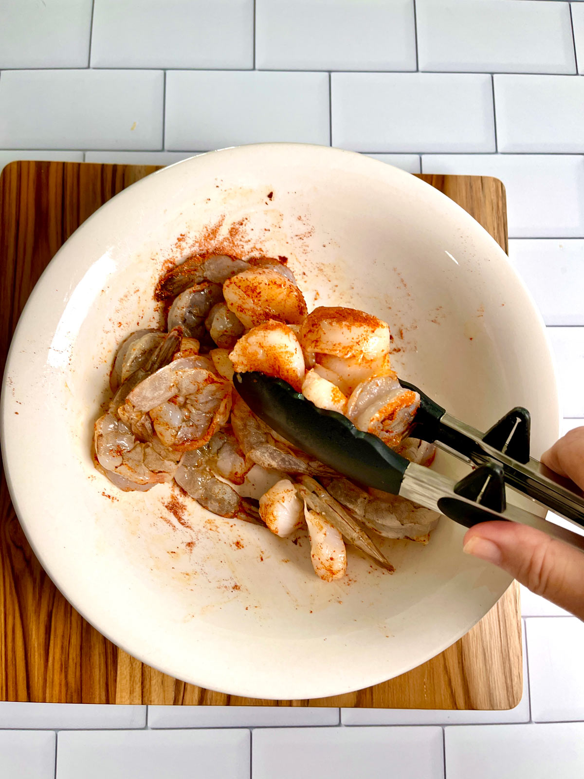 Mixing spices onto shrimp with tongs