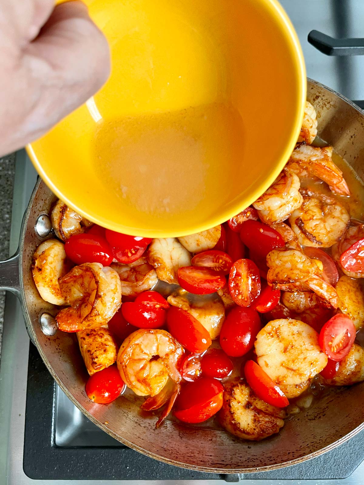Pouring liquids from small bowl into pan with shrimp and scallops