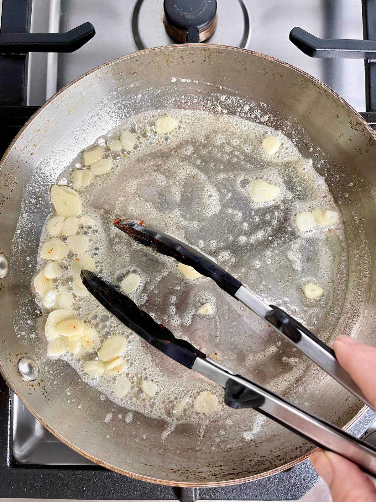 Removing garlic slices from pan with tongs
