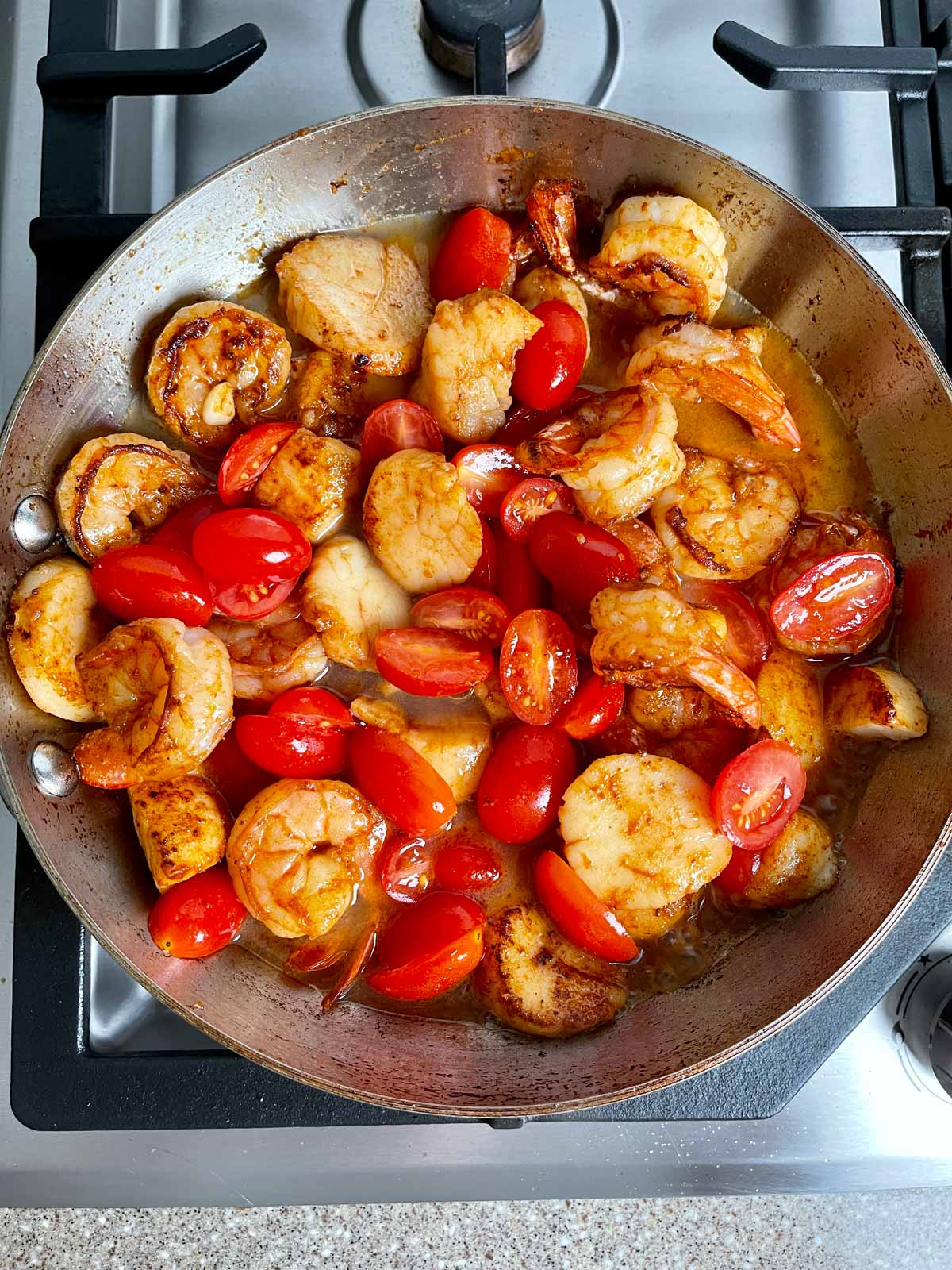 Shrimp, scallops, and tomatoes cooking in broth
