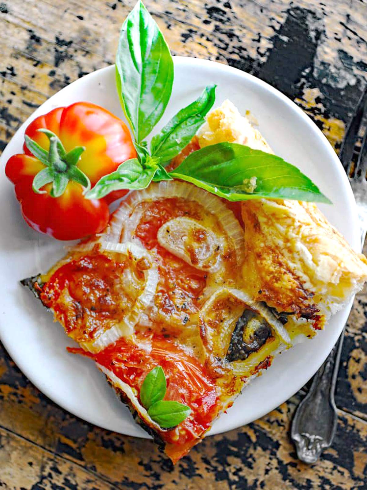 Plate with a square slice of tomato tart with basil and tomato garnish.
