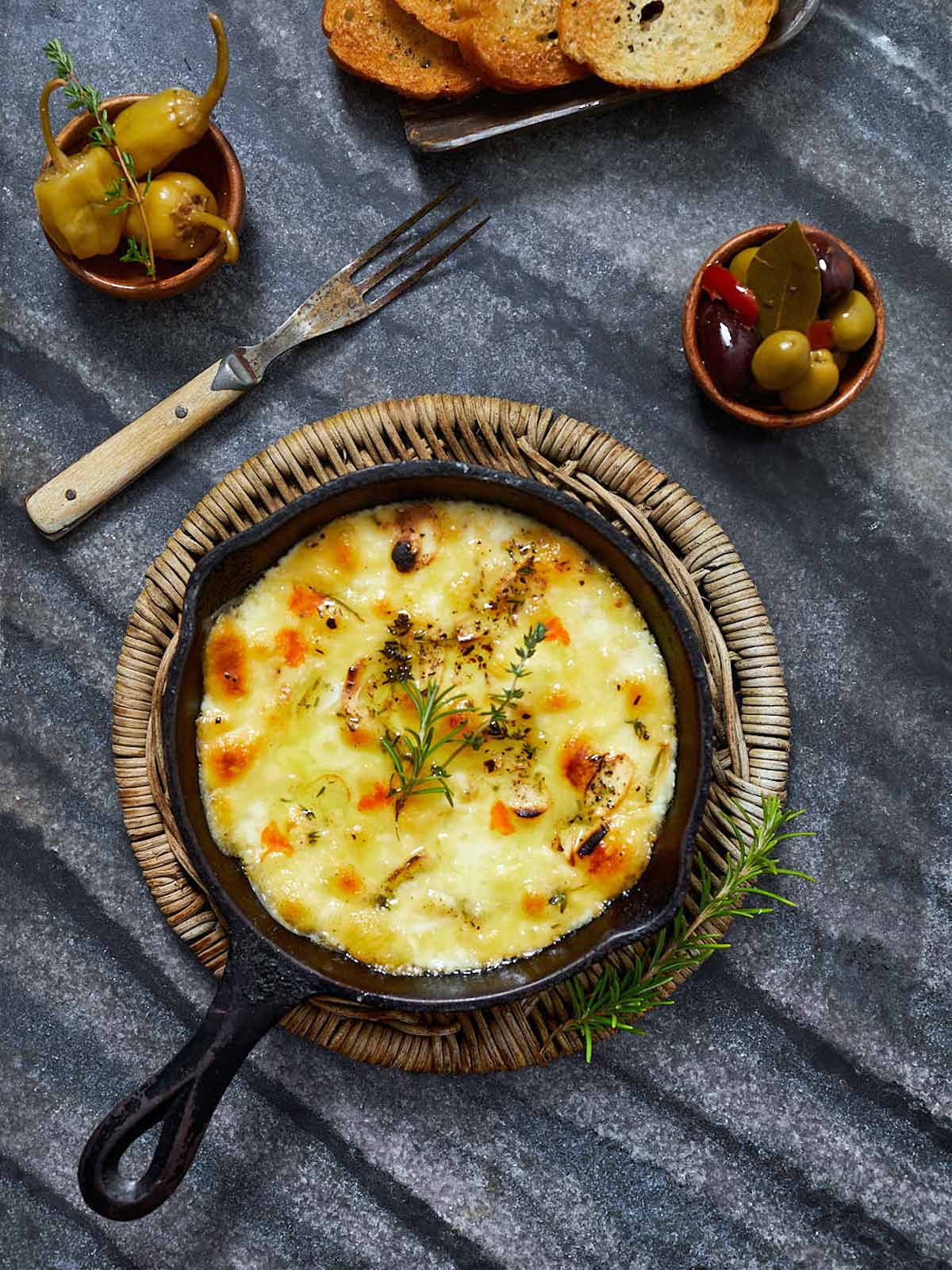 Prepared Baked Fontina Appetizer for Two on trivet with olives, peppers, and toasted French baguette.