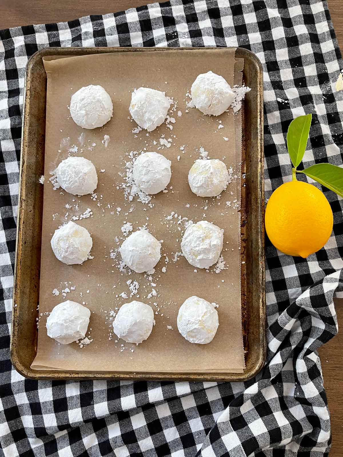 Powdered sugar coated dough balls on baking sheet ready for oven.