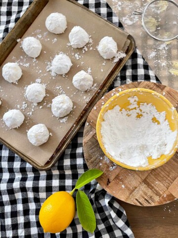 Dough balls covered in powdered sugar on parchment lined baking sheet.