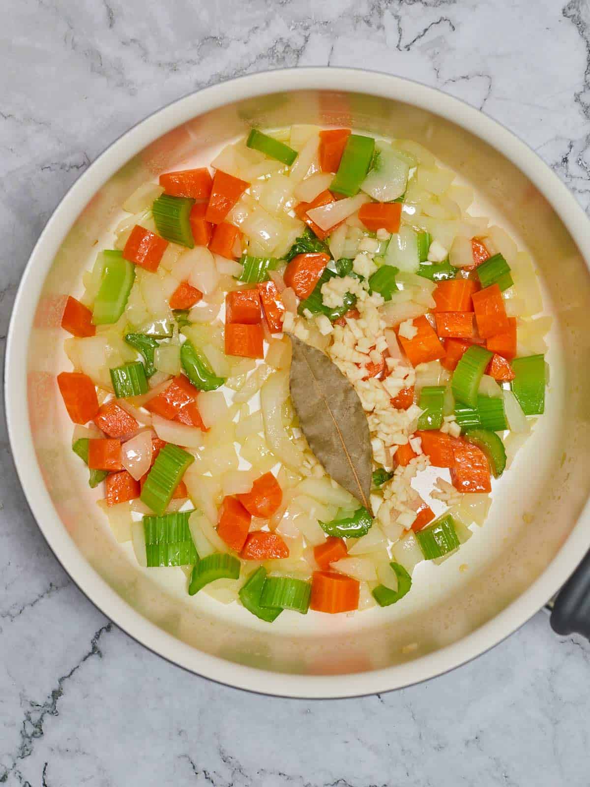 Cooked vegetables with bay leaf added to skillet.