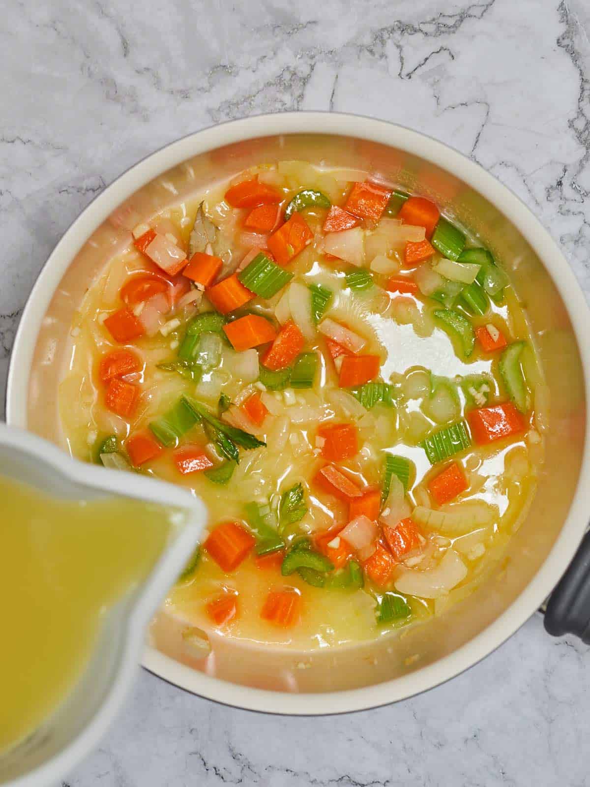 Broth being poured into the skillet with the cooked vegetables.