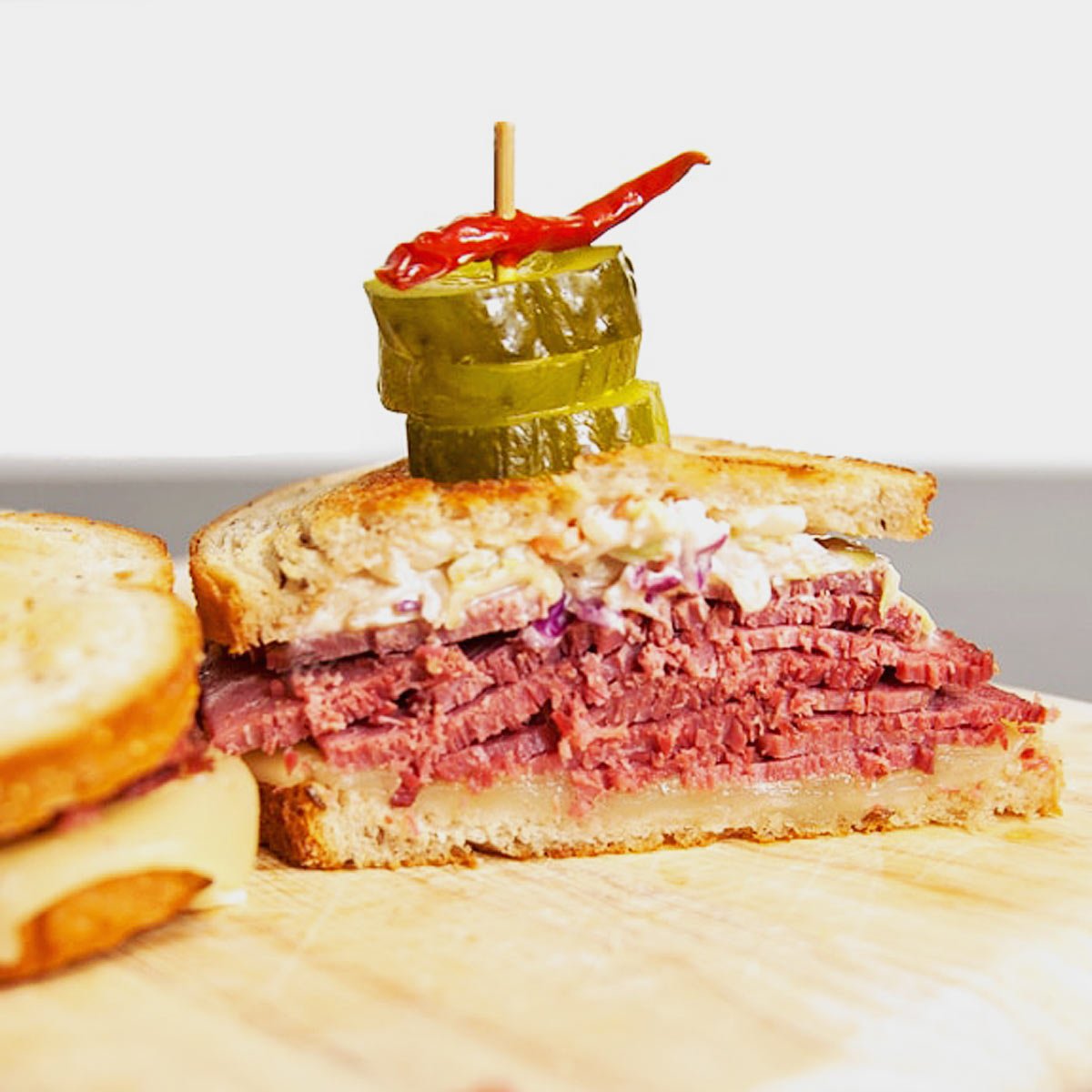 A sandwich with meat and pickles served on a wooden cutting board, accompanied by a flavorful Reuben sauce.