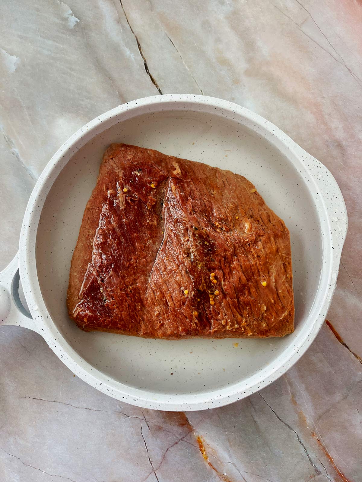 Corned beef in a shallow pan with water.