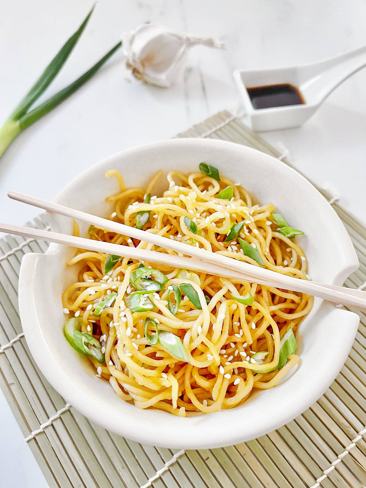 Picture of a bowl of noodles with green onion garnish and chopsticks.