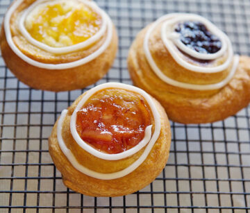 Picture of three rolled up pastries with fruit filling and glaze swirled on edge.