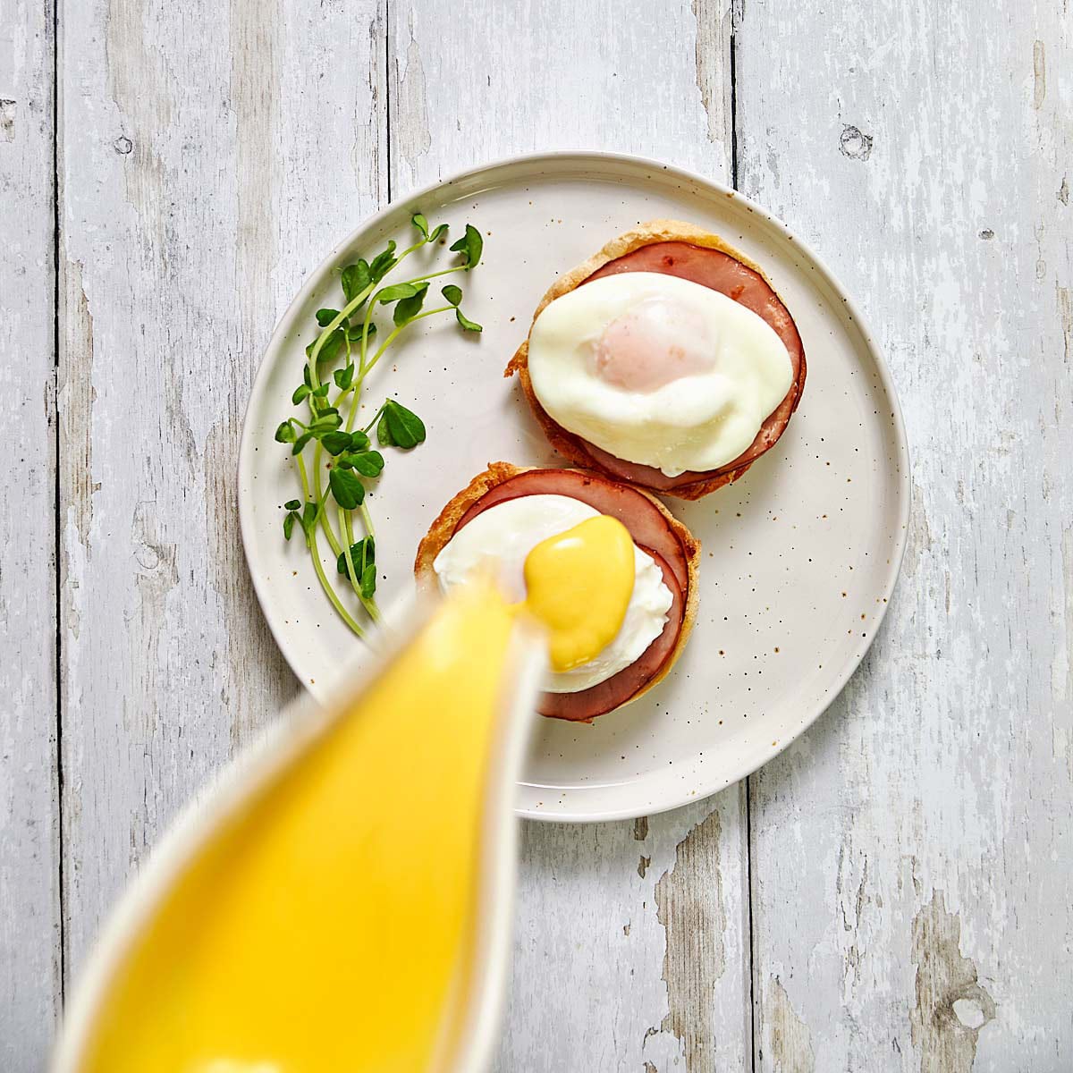 Pouring Hollandaise sauce from small pitcher onto poached eggs.