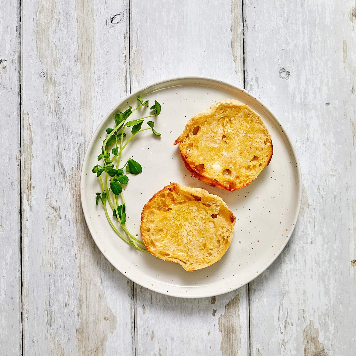 Plate with two halve of a toasted English muffin with butter