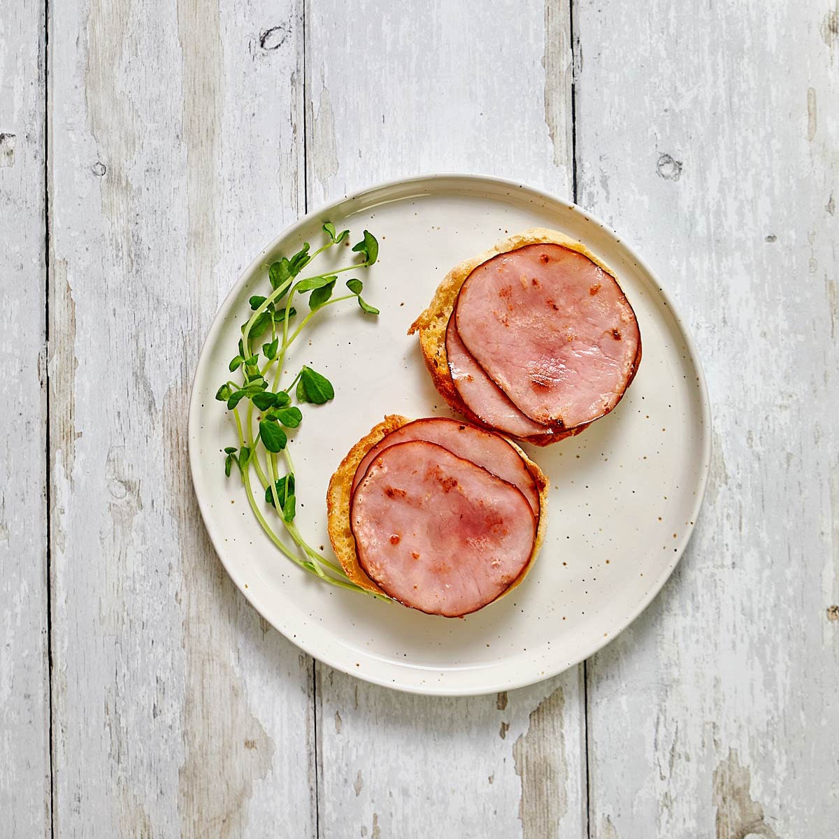Plate with two halves of English muffin with Canadian bacon added.