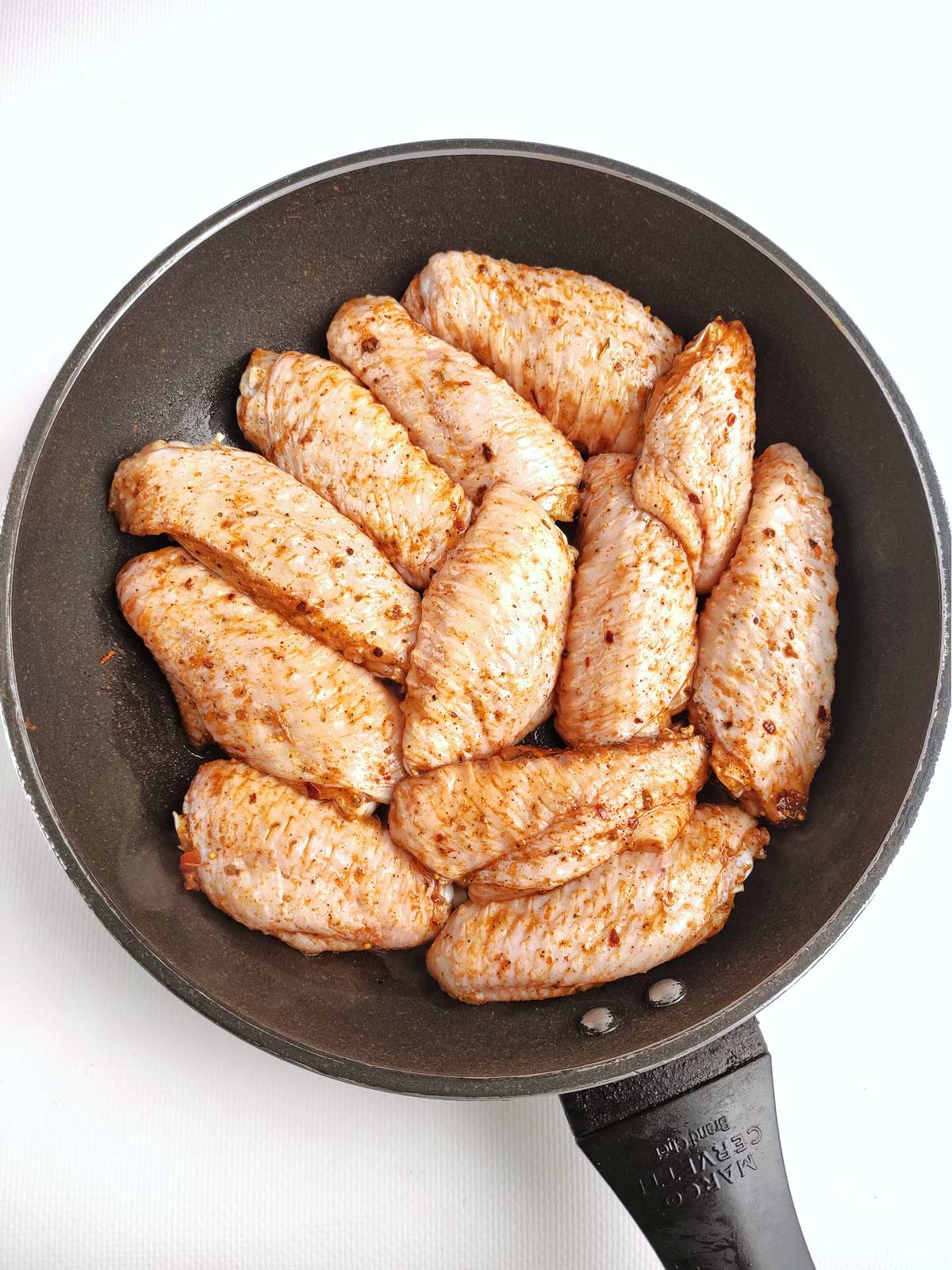 Chicken wings in oil in skillet.