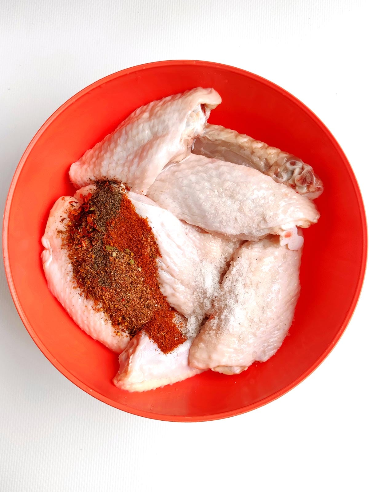 Red bowl with chicken wings and dried spices.