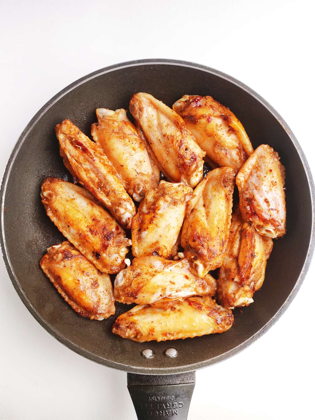 Chicken wings in skillet browned on one side.