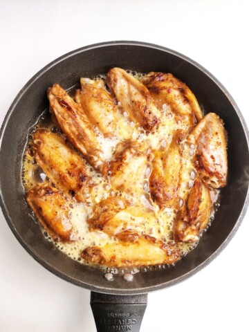 Cooked chicken wings in skillet with beer bubbling hot.