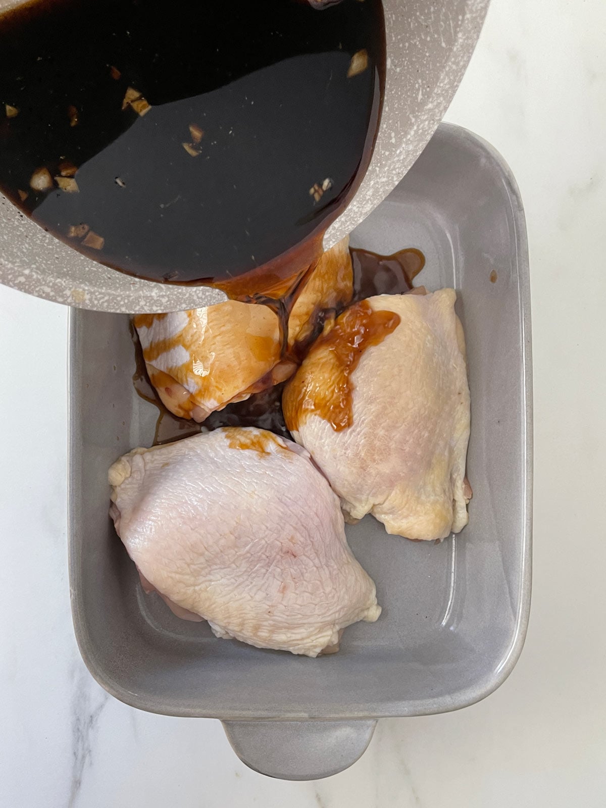 Sauce poured over chicken thighs in baking dish.