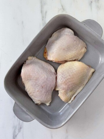 Three chicken thighs in a grey rectangle baking dish.